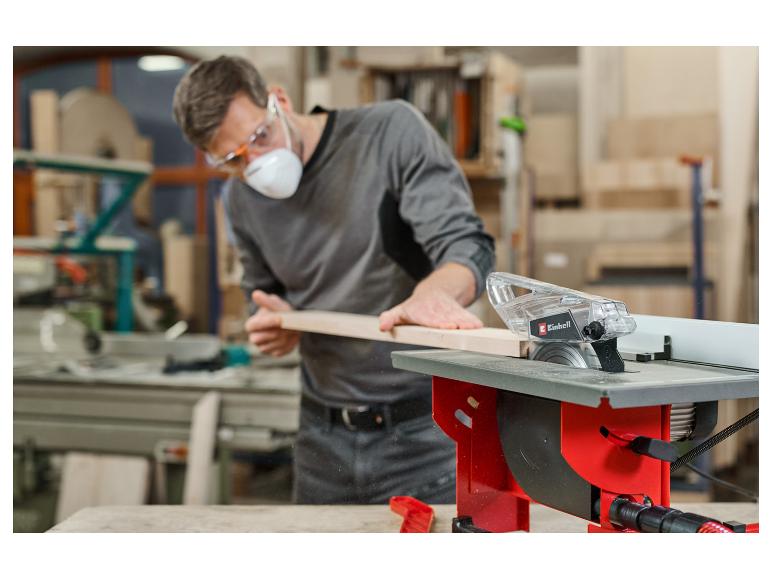 Mann in Schutzkleidung sägt Holz mit einer Tischkreissäge in einer Werkstatt