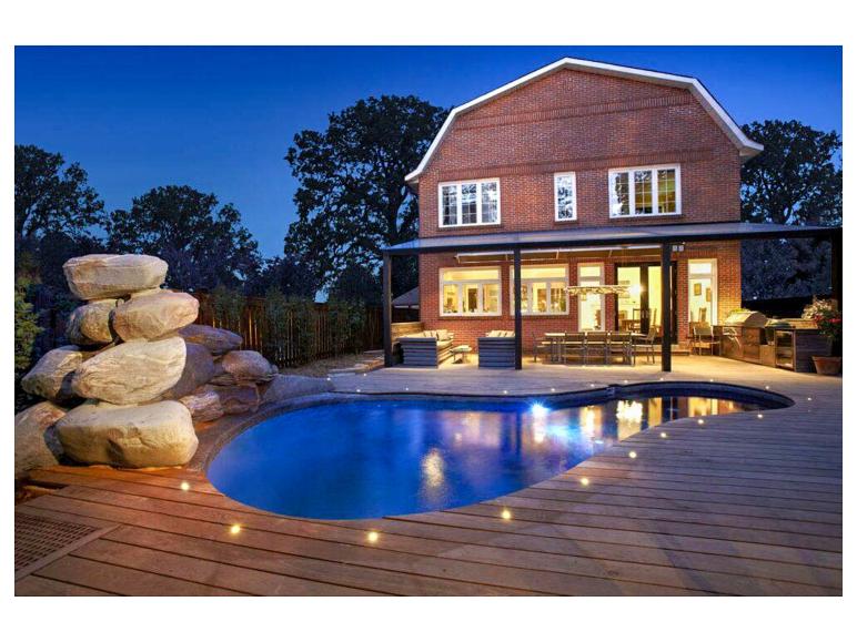 Backsteinhaus mit Pool und beleuchteter Holzterrasse bei Nacht.