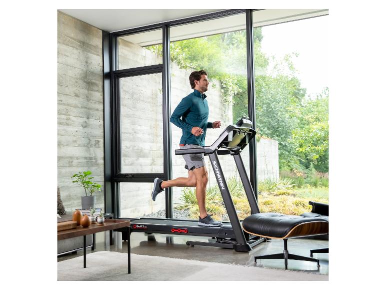 Mann trainiert auf einem Laufband in einem modernen Raum mit großen Fenstern.