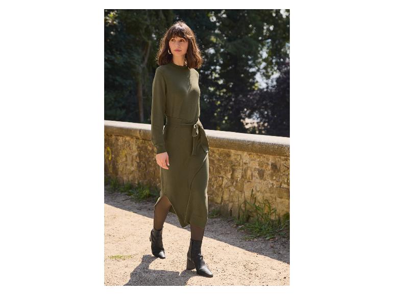 Frau in einem olivgrünen Midikleid mit schwarzen Stiefeln geht auf einem Weg.