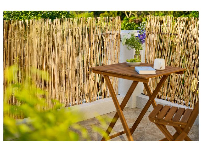 Balkon mit Bambuszaun, Holztisch und Stuhl, Blumen und Buch.