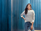 Eine Frau trägt einen gestreiften Pullover und blaue Jeans vor einem blauen Hintergrund.