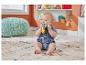 Ein Baby in einem Jeans-Strampler sitzt auf einem gemusterten Teppich und kaut auf einem bunten Beißring.