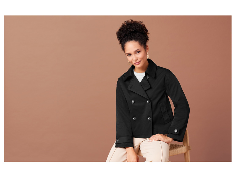 Eine Frau trägt einen schwarzen Mantel und eine beige Hose.