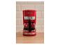 Rote Kaffeemaschine mit Glaskanne voller Kaffee, auf einer Holztheke.