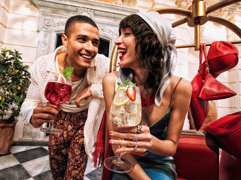 Paar mit Cocktails und roten Taschen im Freien.