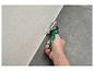 Hand schneidet eine weiße Dichtungsraupe zwischen heller Wand und dunklem Boden mit grünem Werkzeug.