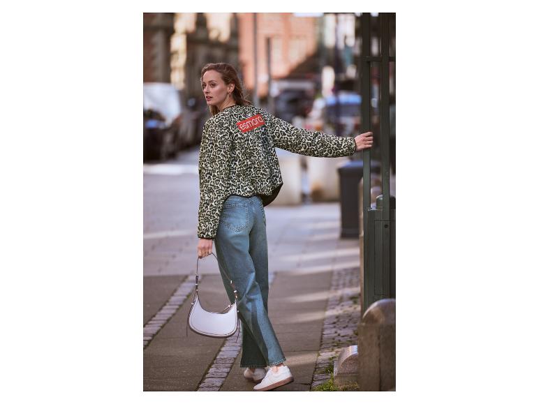 Eine Frau in Leopardenjacke und Jeans hält eine weiße Handtasche auf einer Stadtstraße.