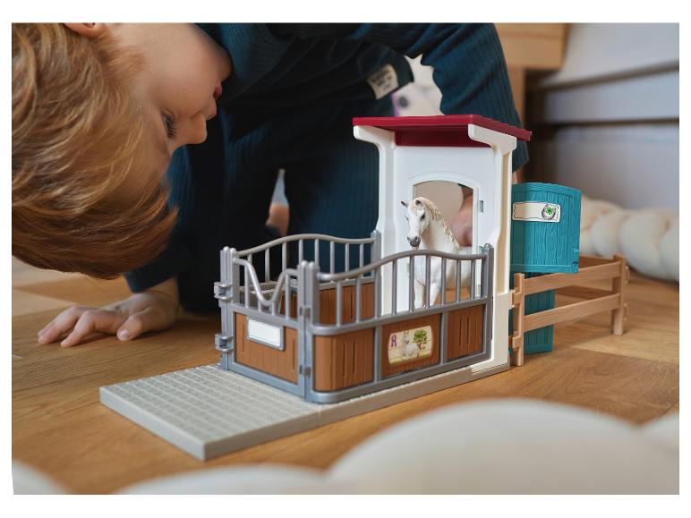 Kind spielt mit Spielzeug-Pferdestall mit weißem Pferd auf Holzboden.