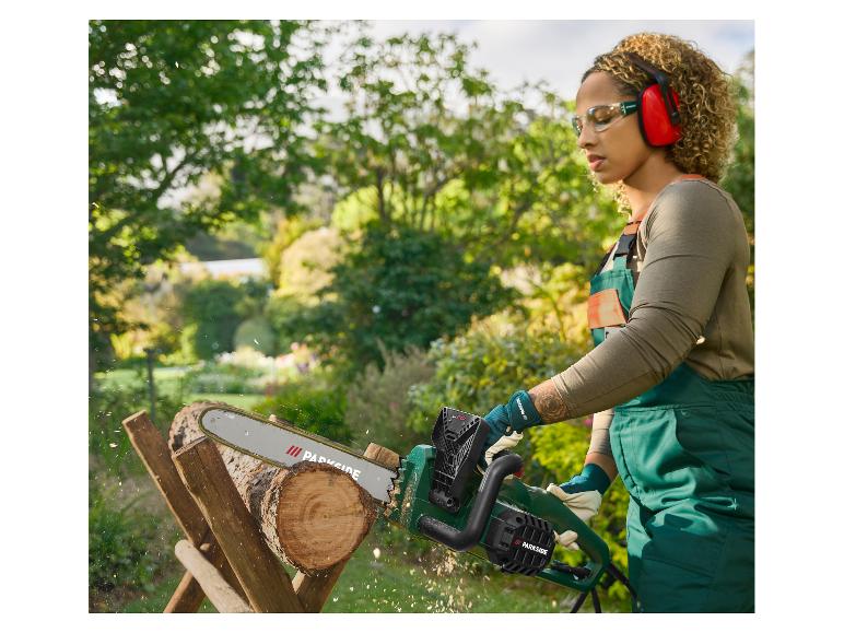 Frau in Schutzkleidung schneidet Holz mit einer Parkside Kettensäge im Garten.