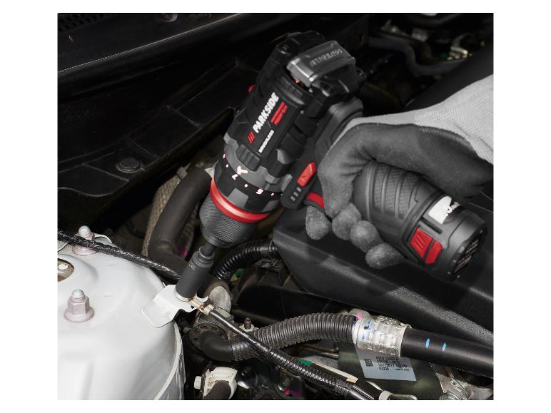 Eine Person benutzt einen Akkuschrauber, um an einem Automotor zu arbeiten.