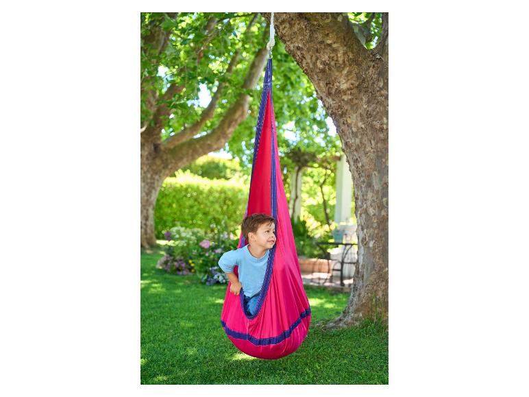 Kind in einer roten Nestschaukel im Garten.