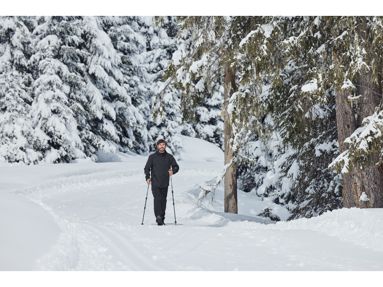 Mann beim Langlaufen mit Stöcken auf einem verschneiten Weg durch einen Winterwald.