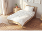 Weiße gesteppte Bettdecke und Kissen auf einem Holzbett in einem hellen Schlafzimmer.