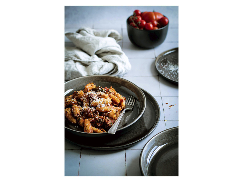 Pasta mit Tomatensauce, Käse und einer Gabel auf einem schwarzen Teller.