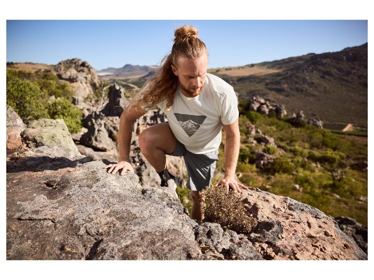 Mann in Sport-T-Shirt und Shorts klettert in den Bergen auf Felsen.