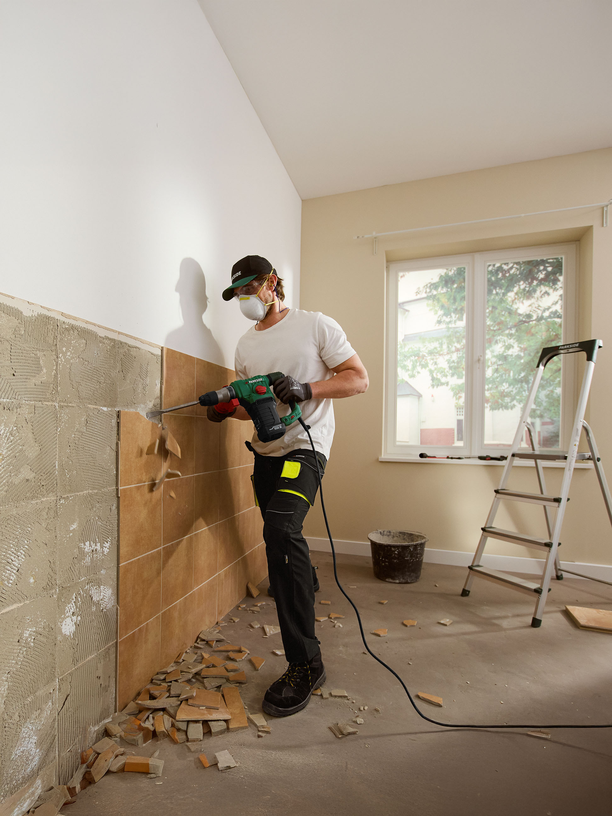 Mann entfernt Fliesen von einer Wand mit einem Parkside Bohrhammer.