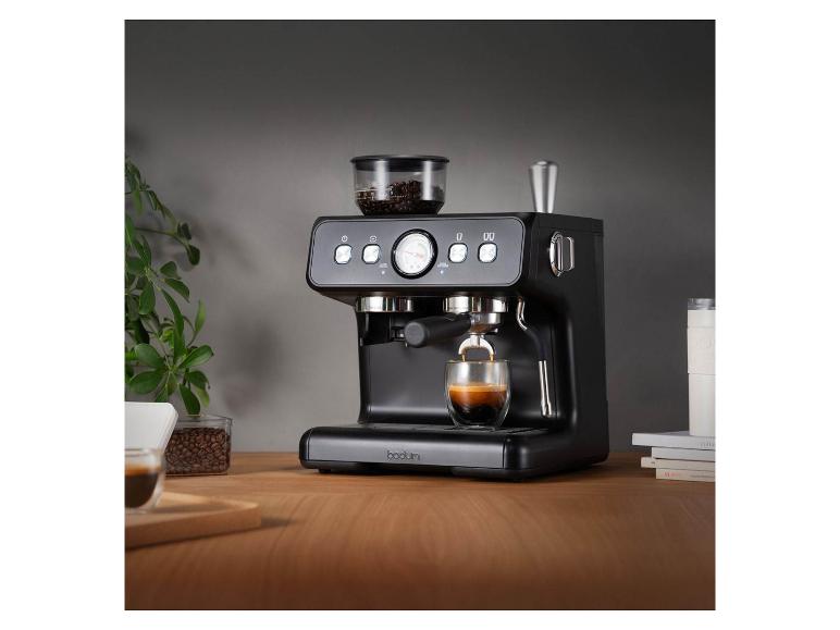 Schwarze Espressomaschine mit Kaffeebohnen und einem Glas Espresso auf einem Holztisch.