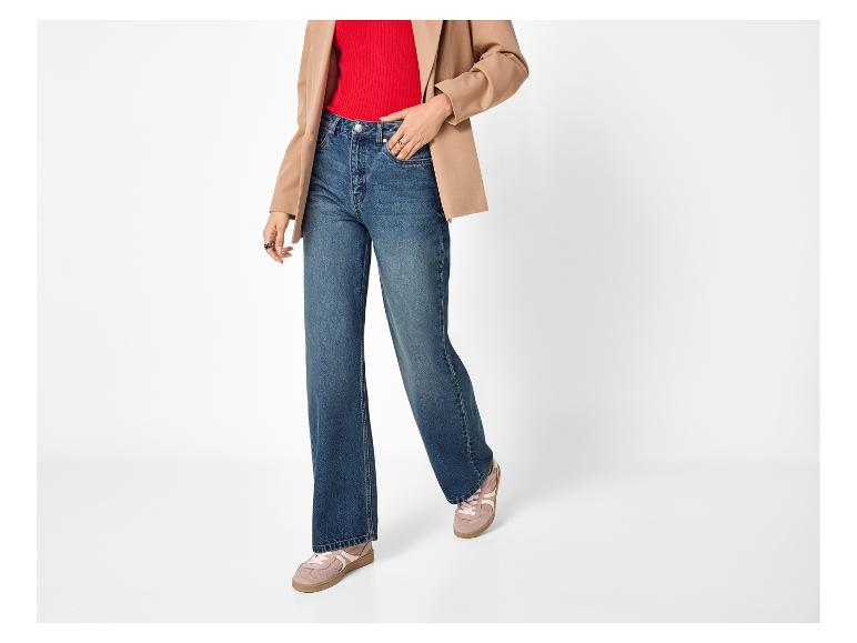 Frau in rotem Top, beigem Blazer, blauen Jeans und rosa Sneakern.