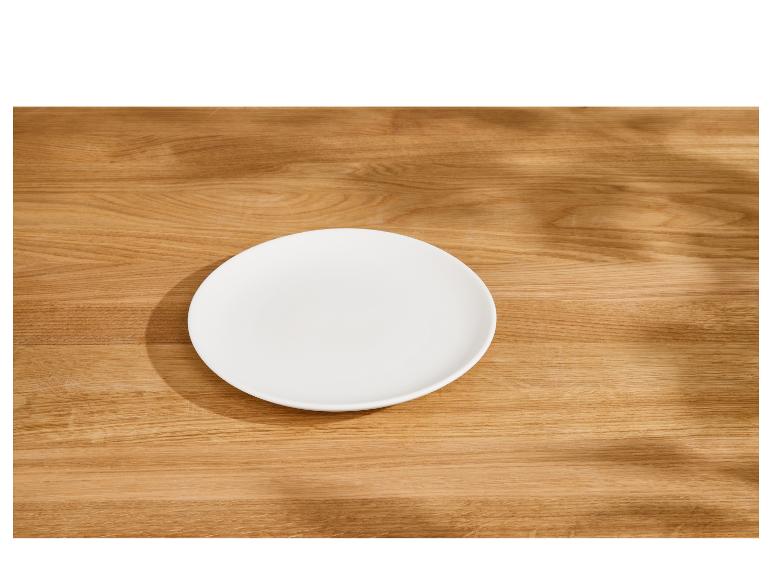 Leerer weißer Teller auf einem Holztisch mit Blattschatten