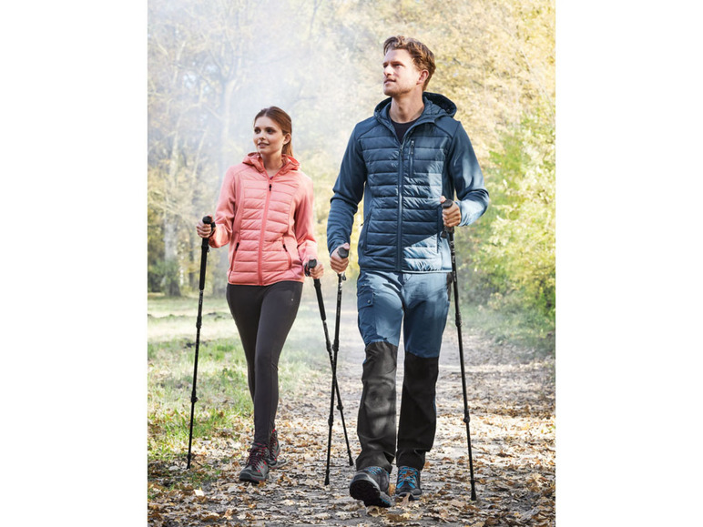 Zwei Personen wandern mit Wanderstöcken und Winterjacken im Wald.