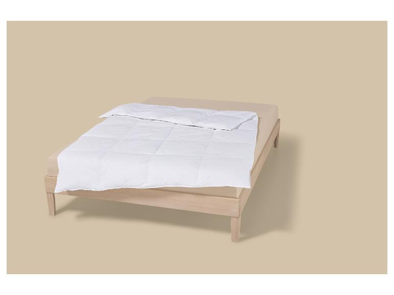 Weiße Bettdecke zusammengefaltet auf einem hellbraunen Bett mit Holzrahmen.