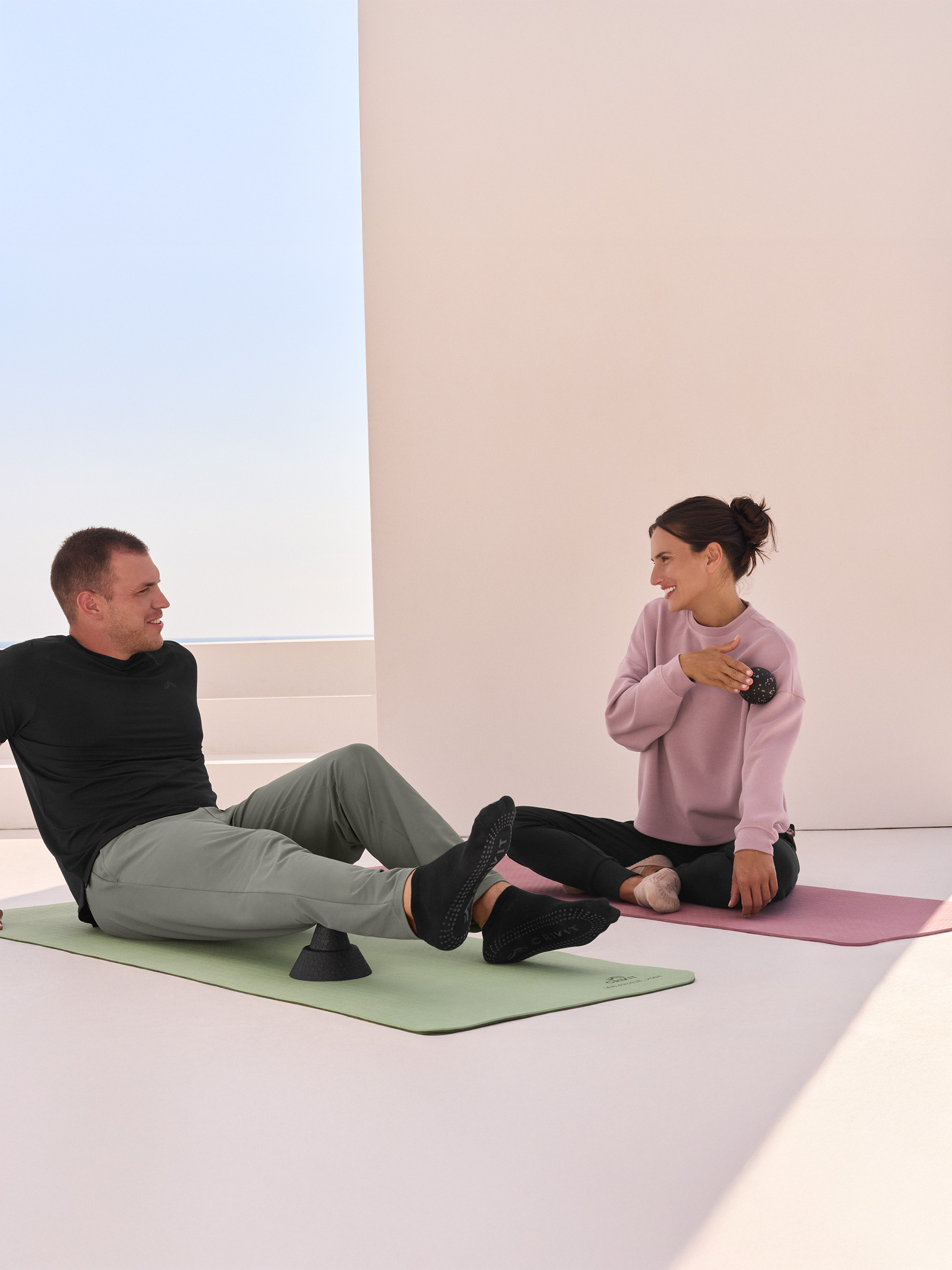 Zwei Personen auf Yogamatten, der Mann benutzt eine Massagerolle, die Frau einen Massageball.