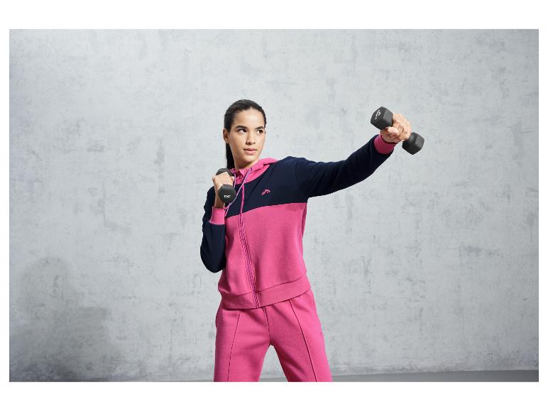 Eine Frau in einem rosafarbenen Trainingsanzug mit Kapuze trainiert mit Hanteln.