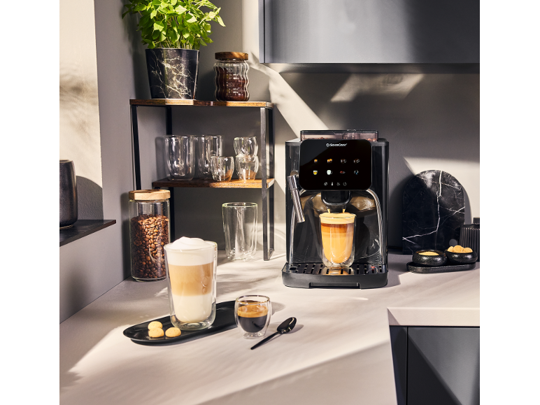 Kaffeemaschine mit zwei Tassen Kaffee, Kaffeebohnen und einer Pflanze in der Küche.