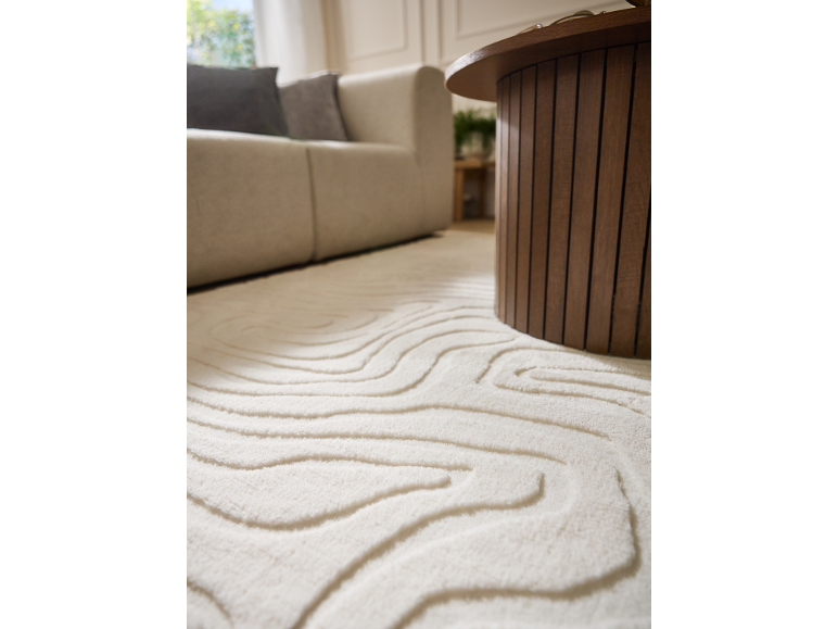 Weißer strukturierter Teppich mit Wellenmustern, beiges Sofa und Couchtisch aus Holz.
