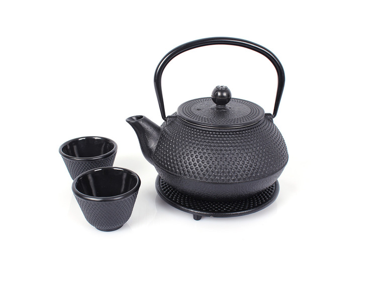 Eine schwarze gusseiserne Teekanne mit zwei Tassen und einem Untersetzer.