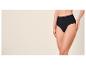 Frau in schwarzem High-Waist-Slip vor beigem Hintergrund.