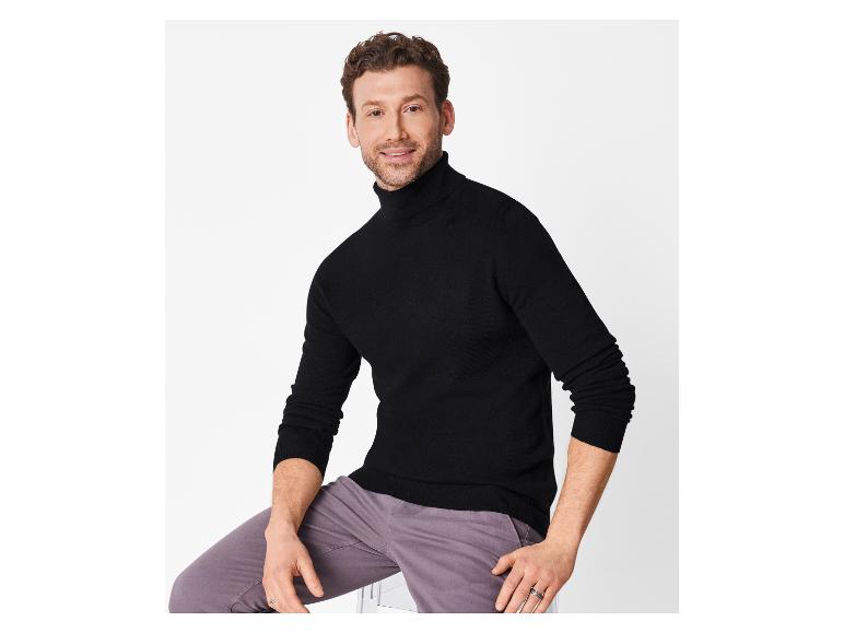 Lächelnder Mann in schwarzem Rollkragenpullover und grauer Hose.