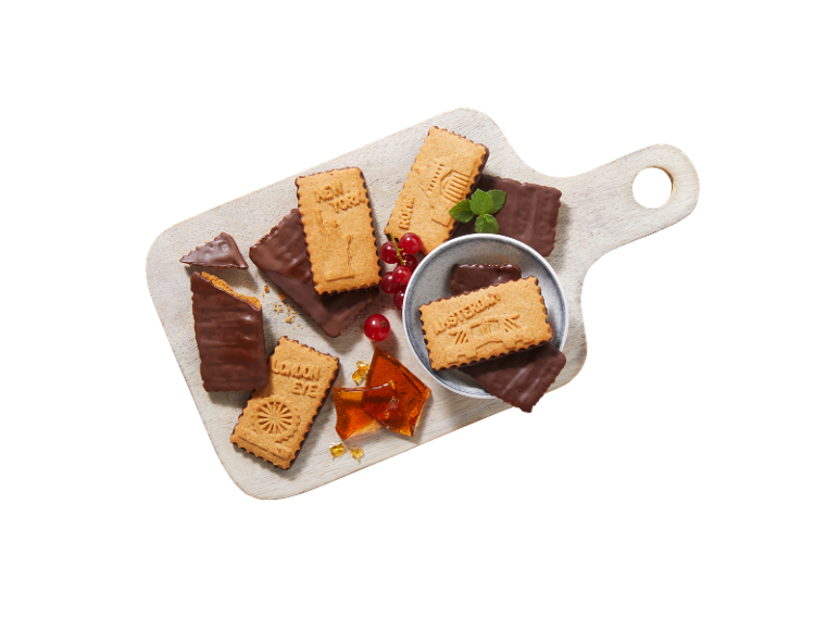 Holzschneidebrett mit schokoladenüberzogenen Keksen mit Stadtmotiven, roten Johannisbeeren und Karamellstücken.