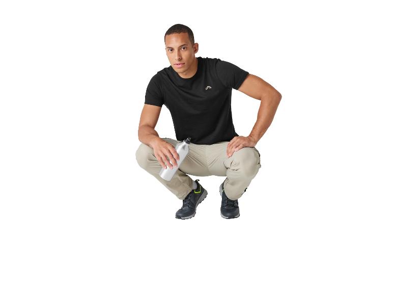 Mann in schwarzem T-Shirt, beiger Hose und Wanderschuhen, hält eine Wasserflasche.
