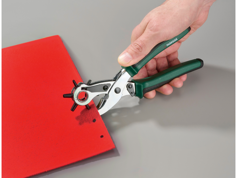 Hand hält eine Revolverlochzange, die Löcher in rotes Material stanzt.