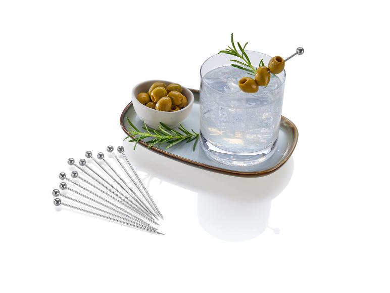 Cocktail mit Eis, Oliven und Rosmarin, ein Set Cocktailspieße und eine Schale Oliven.