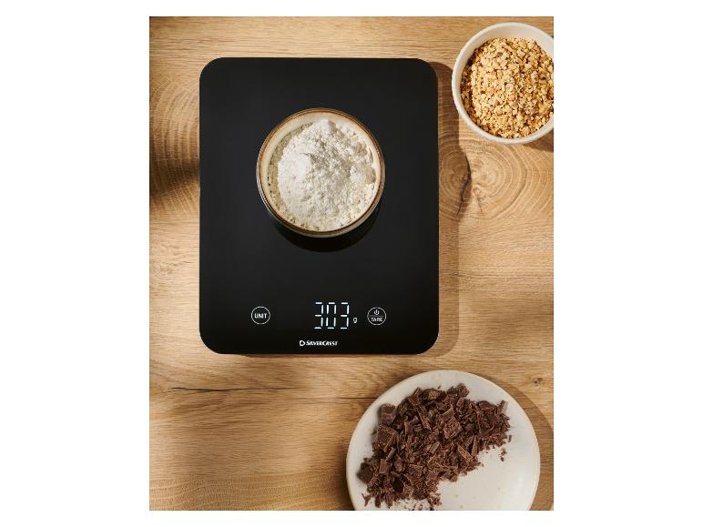 Schwarze digitale Küchenwaage mit einer Schüssel Mehl, gehackten Haselnüssen und Schokolade.