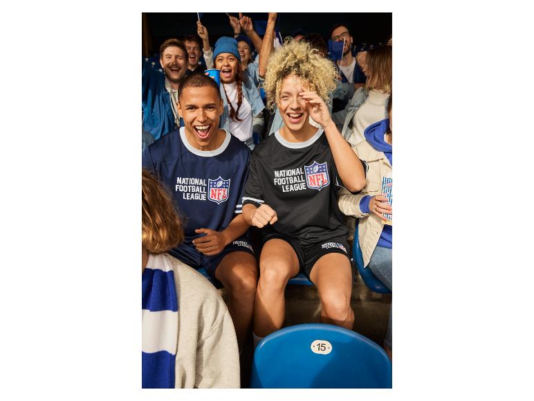 Mann und Frau in NFL-Trikots sitzen im Stadion mit anderen Fans.