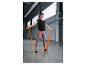 Frau in Sportkleidung mit orangefarbenem Widerstandsband im Fitnessstudio.