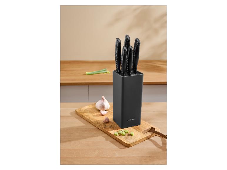 Schwarzer Messerblock mit fünf Messern, Knoblauch und Frühlingszwiebeln auf einem Holzschneidebrett.