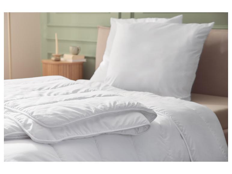 Weiße Bettdecke und Kissen auf einem Bett, mit Schlafzimmerinterieur im Hintergrund.