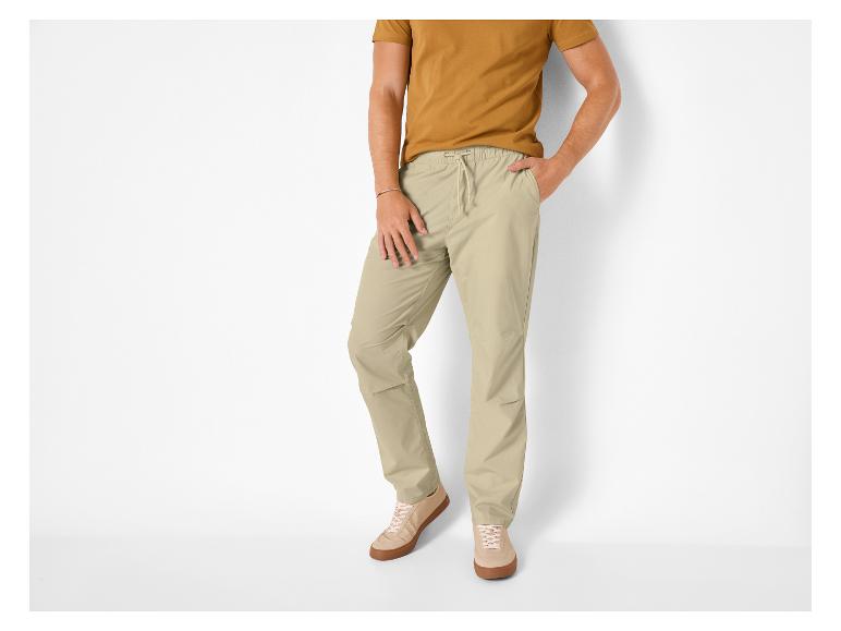Mann in senfgelbem T-Shirt und beiger Kordelzug-Hose, beige Sneaker.