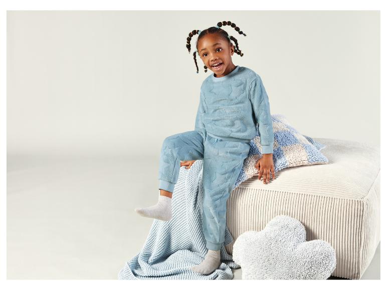 Ein Mädchen trägt einen blauen Schlafanzug mit Sternenmuster und sitzt auf einem Sofa mit Kissen.