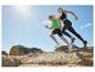 Zwei Athleten laufen über Felsen unter blauem Himmel, tragen Sportkleidung und Laufschuhe.