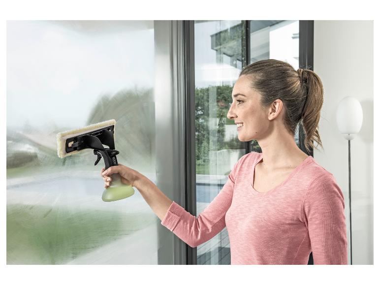 Frau reinigt ein Fenster mit Fensterreiniger und Sprühflasche.