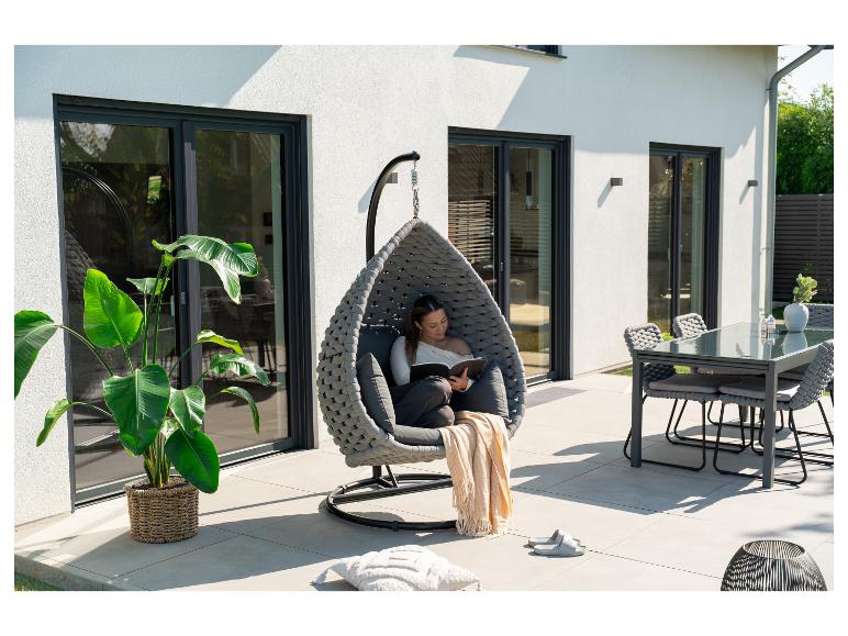 Frau liest in einem Hängesessel auf einer Terrasse mit Esstisch und Pflanzen.