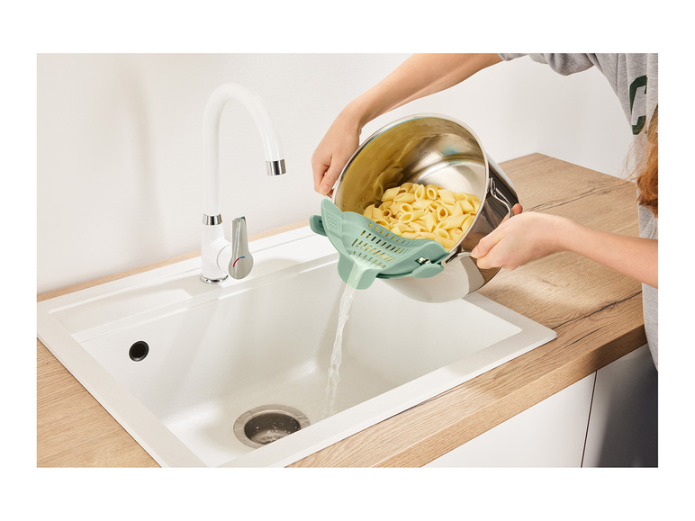 Eine Person gießt gekochte Pasta aus einem Topf mit einem Sieb.