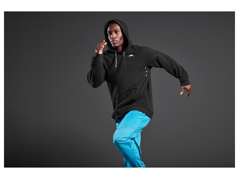 Ein Mann in einem schwarzen Kapuzenpullover und blauen Hosen.