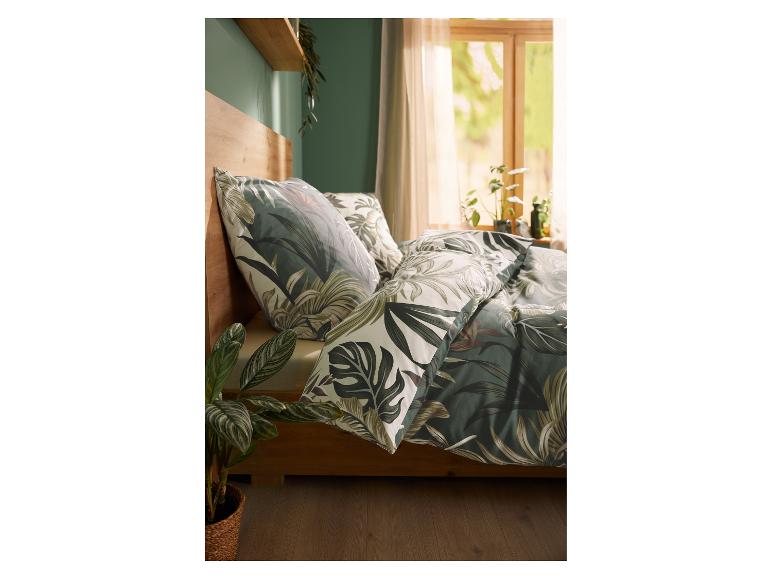 Schlafzimmer mit tropischer Bettwäsche, Pflanzen und grüner Wand.